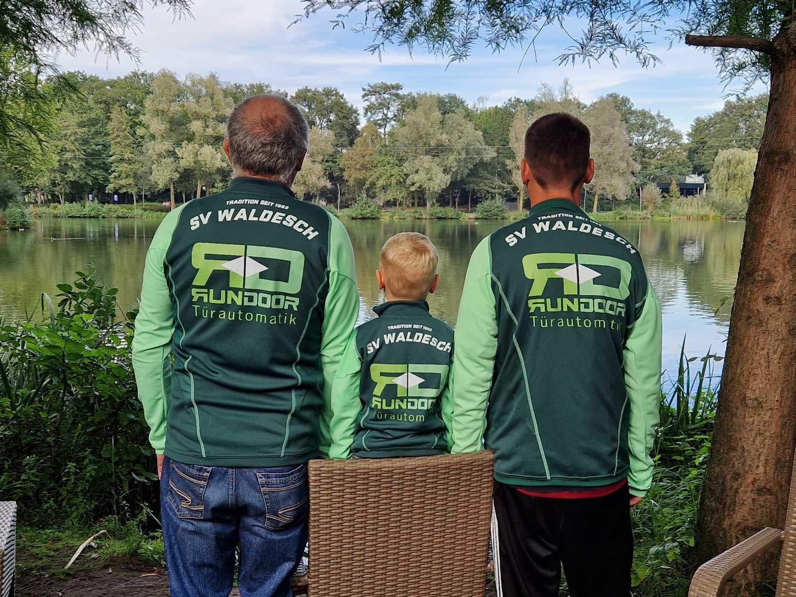 Trikot auf Tour - Drei Generationen: Vater, Sohn und Enkel blicken auf einen See