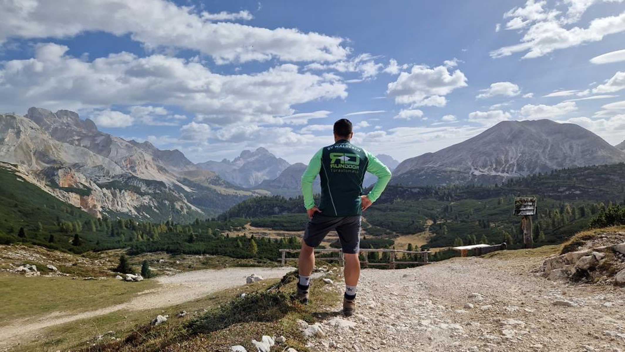 Trikot auf Tour - Junger Mann auf einem Gipfelausblick ganz oben in den Bergen mit Blick auf die Wolken und die Bergspitzen