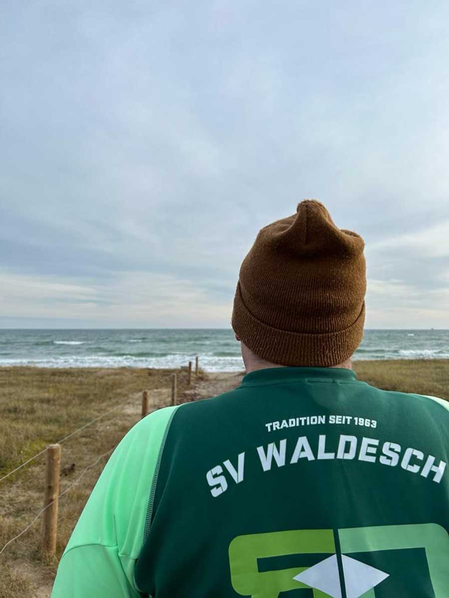 Trikot auf Tour - Ein Mann steht in einer Dünenlandschaft und blickt auf das Meer