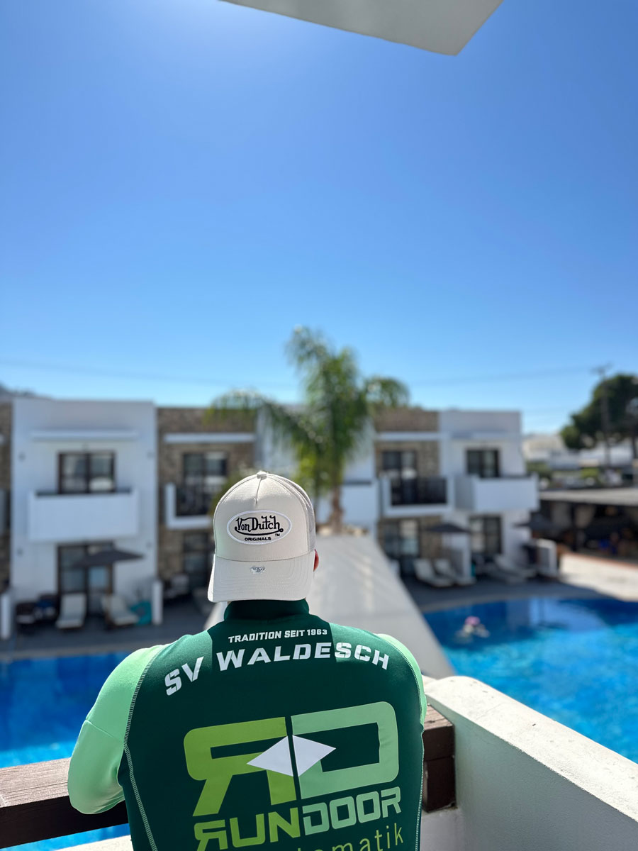 Trikot auf Tour - Mann blickt von einem Balkon in einer südlichen Wohnanlage auf den Pool